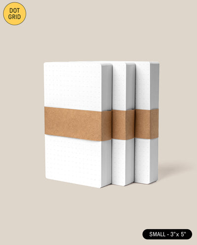 Three small Analog Dot Grid Cards notebooks (3x5, white covers) are stacked upright and wrapped with a brown paper band, set against a plain beige background. Perfect for fans of analog dot grid cards. 3-Pack included.