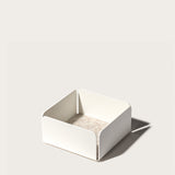 The Gather 2x2 Organizer Set (White) is a minimalist, powder-coated steel organizer with a square shape, rounded corners, and low sides. It features a light beige base and casts a right-side shadow on a plain background.