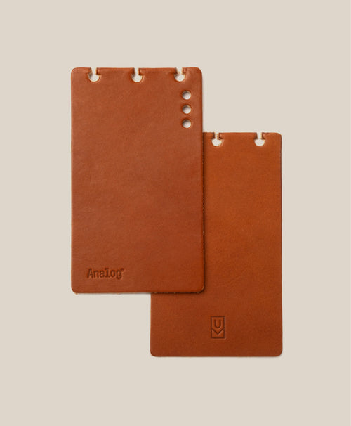 Two tan full-grain leather *Covers Only* – Leather Discbound Analog rest on a beige background. Designed for Discbound Analog systems and made in the USA, one cover features four circular holes and an "AnaLog" stamp, while the other displays three notches with a small logo near its bottom edge.