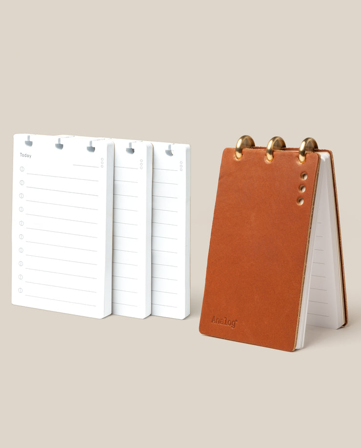 Small open planner with white pages and a brown leather cover on a beige background