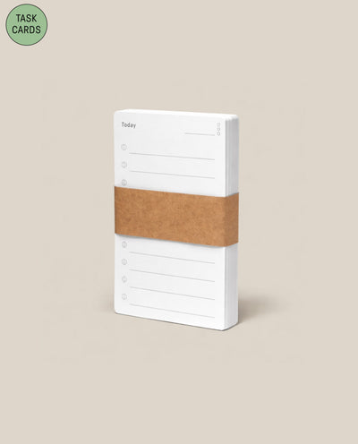 A 1-pack of Analog Task Cards, featuring white cards with "Today" and writing lines, bound by a brown paper band. A green circle at the top left reads TASK CARDS—an analog productivity tool set against a beige background.
