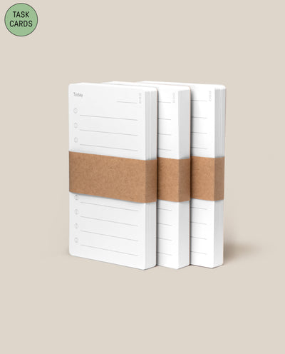 Three stacks of Analog - Task Cards (3-Pack), each bound with a brown paper band, are displayed on a beige background. A green circle in the top left highlights them as an analog productivity system called TASK CARDS.