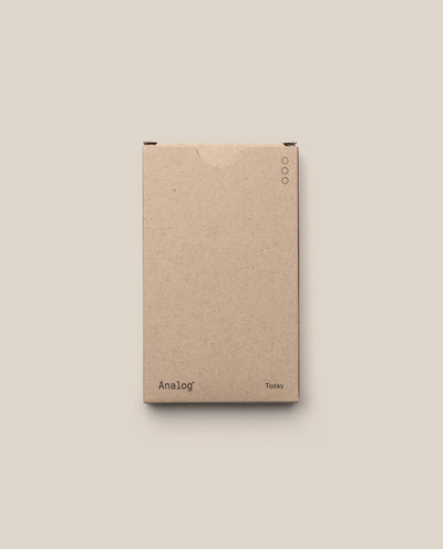 A plain brown cardboard box labeled "Analog" (lower left) and "Today" (lower right), with three circles near the top right, contains Analog - Today Cards (1-Pack) for prioritizing tasks, shown against a beige background.