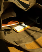 Interior view of a sturdy olive Ugmonk Utility Tote (Olive) containing a notebook, a yellow folder, a black rolled object, and a set of keys.