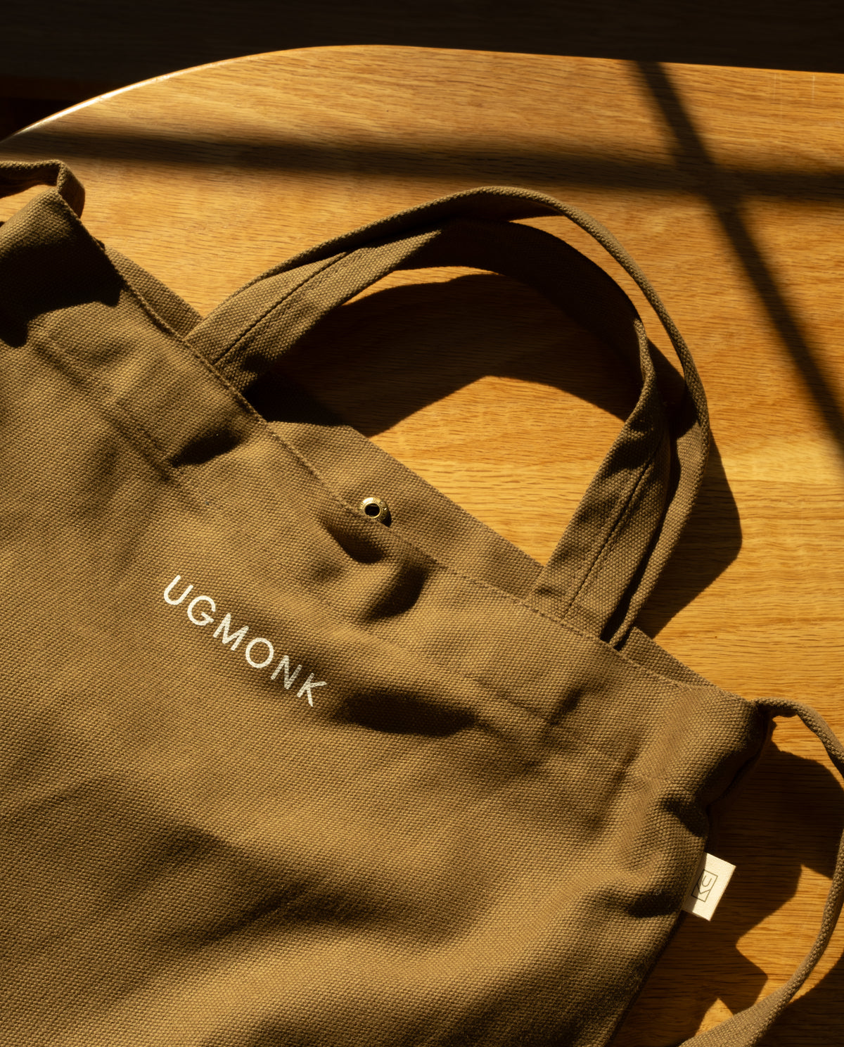 Sturdy olive green Ugmonk Utility Tote (Olive) canvas bag with a snap closure and the word UGMONK printed in white.