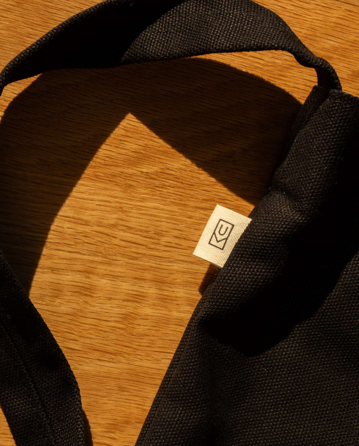 Sturdy heavyweight black Ugmonk Utility Tote featuring a small woven tag with a line-art logo on a wooden surface.