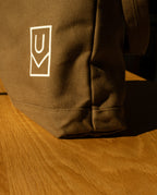A brown heavyweight cotton canvas Utility Tote Bundle - Set of 3 featuring a white U-shaped logo, resting on a wooden surface.