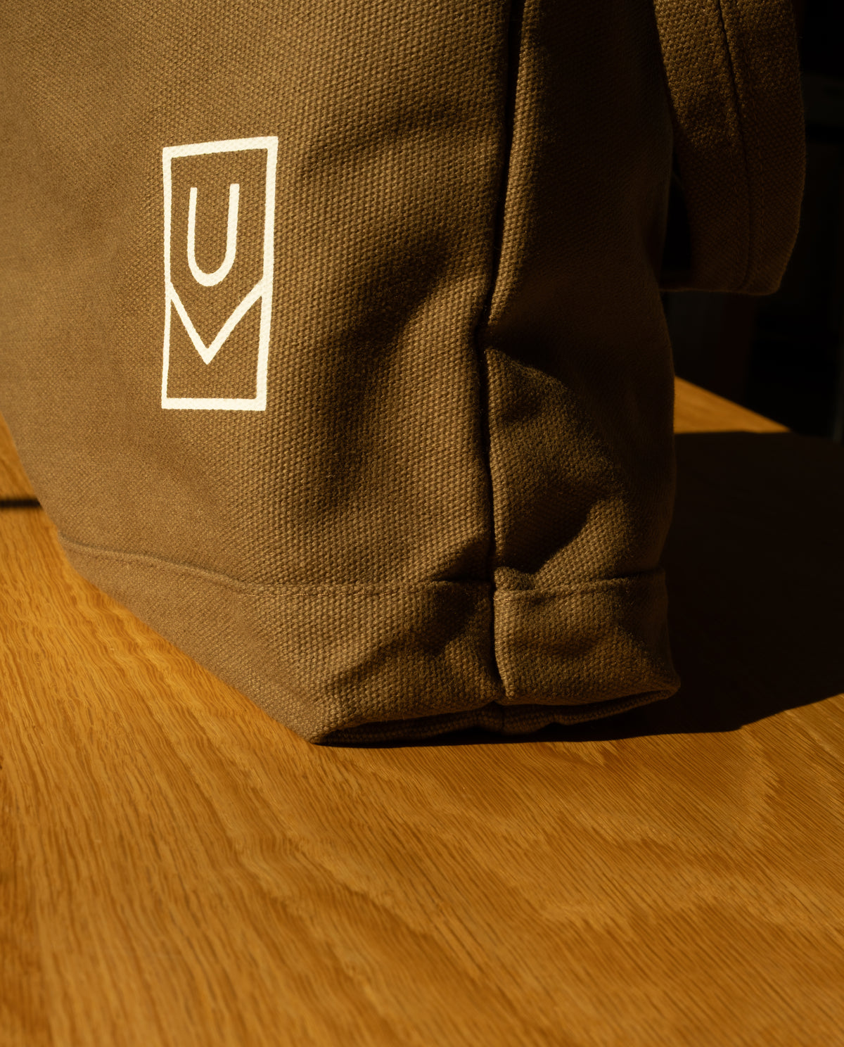 A brown heavyweight cotton canvas Utility Tote Bundle - Set of 3 featuring a white U-shaped logo, resting on a wooden surface.