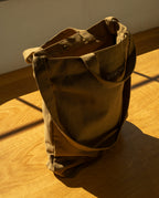 Sturdy olive green Ugmonk Utility Tote (Olive) canvas bag with shoulder straps, shown sitting on a wooden surface.