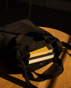 A durable black canvas Utility Tote Bundle - Set of 3 containing two hardcover books sits on a wooden table.