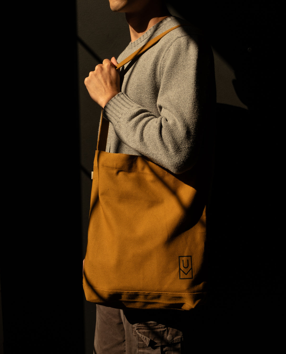 A person carries a large, brown heavyweight cotton Utility Tote Bundle - Set of 3 over their shoulder, featuring a small logo on the lower corner.