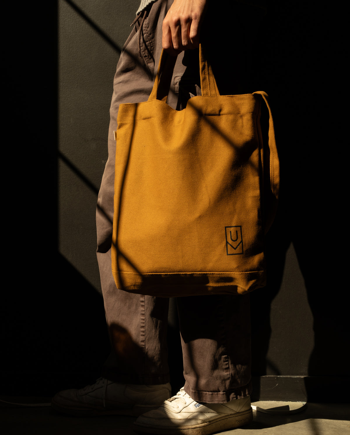 A person holding a mustard yellow heavyweight cotton Utility Tote Bundle - Set of 3 with a small logo on the front.