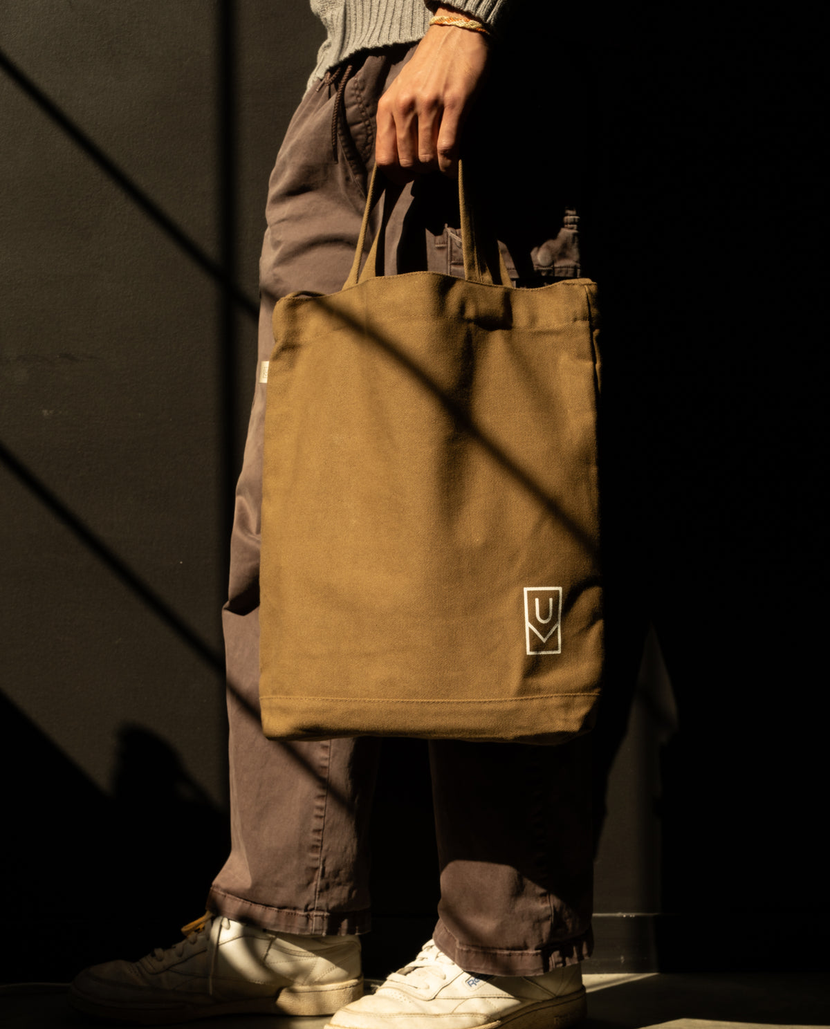 A person holding a sturdy olive Ugmonk Utility Tote (Olive) canvas bag with a small white logo in the corner.