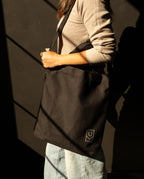 A person wearing a durable, black canvas Utility Tote Bundle - Set of 3 over their shoulder.