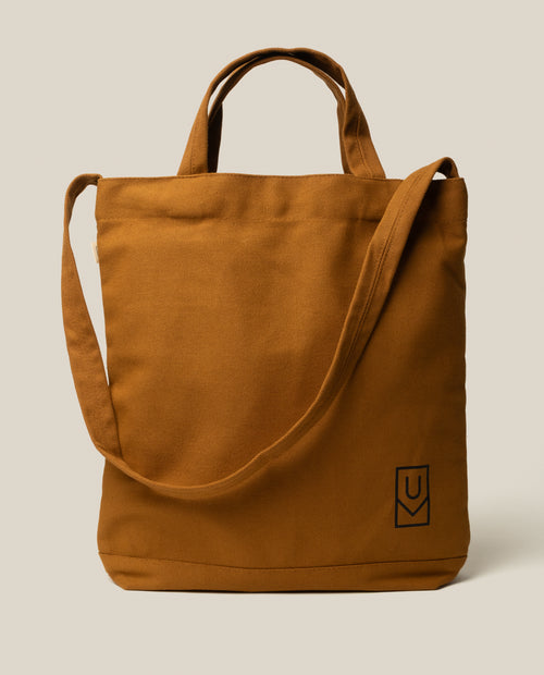 Sturdy tan Ugmonk Utility Tote (Field Tan) canvas bag with two top handles, a shoulder strap, and a small square logo in the bottom corner.