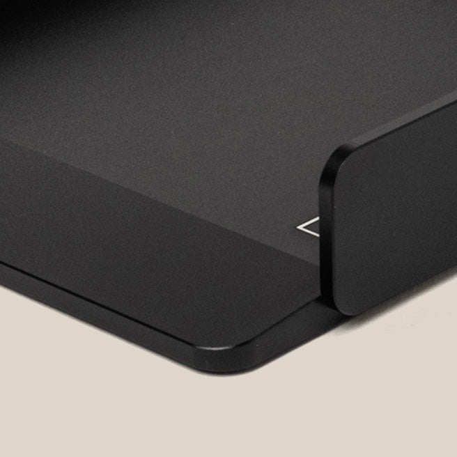 Close-up of a sleek, black, metal desk organizer tray on a light beige surface, showing clean, minimalist lines and a slightly raised edge on one side.