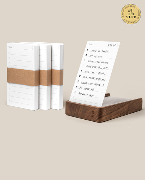 The Analog Daily Focus Kit + 3 Refills (Walnut) features minimalist planner notepads with brown paper bands, a sheet displayed upright in a walnut card holder with a handwritten to-do list, and a #1 Best Seller badge in the top corner.