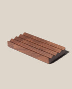 The Gather Wood Zigzag Tray (2x1 - Walnut) is a rectangular solid walnut organizer featuring four evenly spaced, angled grooves, shown on a light beige background.