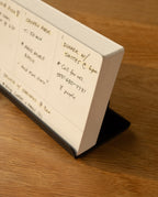 A close-up of an open planner on a wooden surface, showing handwritten dinner plans, a chicken parmesan recipe, and a phone number—organized with weekly cards in the Analog Weekly Kit (Black Steel) card holder.