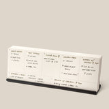 The Analog Weekly Planning Kit (Black Aluminum) is a minimalist desk calendar on a sleek stand, perfect for organizing handwritten meal and event plans like shrimp risotto dinners, takeout nights, and brunch with friends.