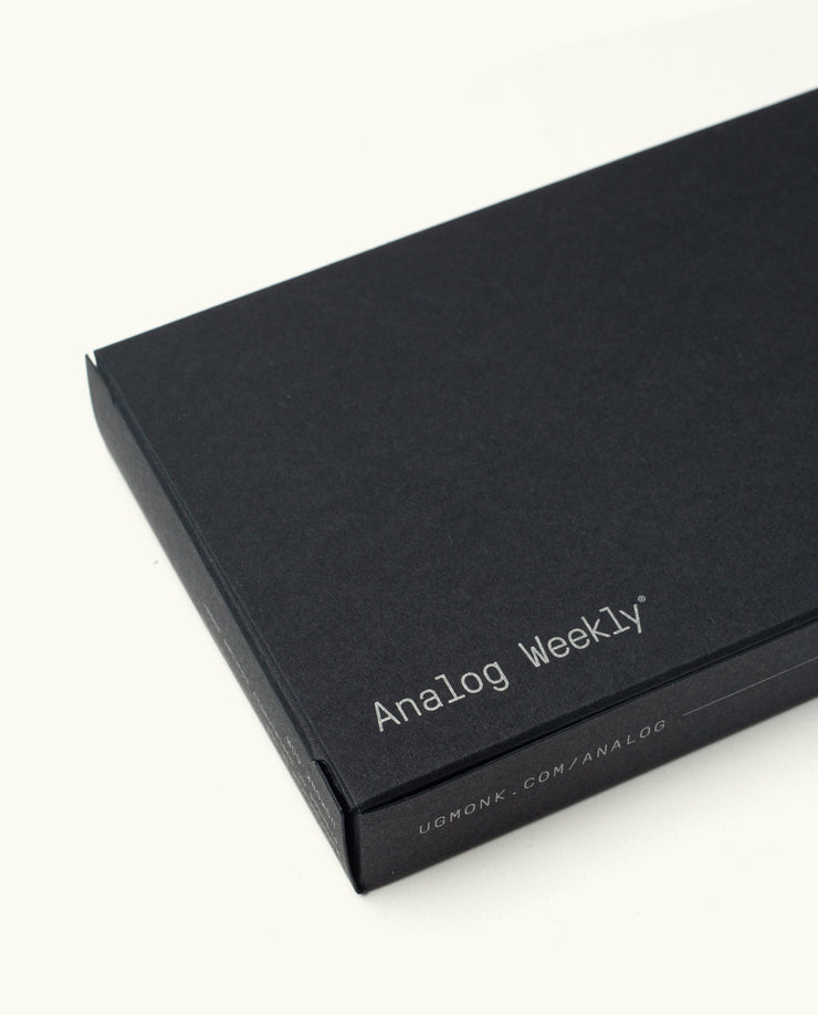 A rectangular black box for the Analog Premium Weekly Kit (Maple), designed to store Weekly Planner Cards, displays "Analog Weekly" in white on the lid and ugmonk.mom/analog on the side, set against a plain white background.