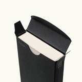 A minimal black cardboard box with a circular cutout partially reveals the edges of Analog Weekly Cards, featuring simple line accents for easy access and a clean design.