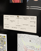 A handwritten weekly schedule is pinned to a black wall, listing tasks like dentist, soccer, inventory, and stables. Children’s colorful drawings are partially visible around the schedule, creating a playful display that pairs perfectly with the Analog Weekly Planning Kit (Walnut) to keep your weekly planner cards organized.