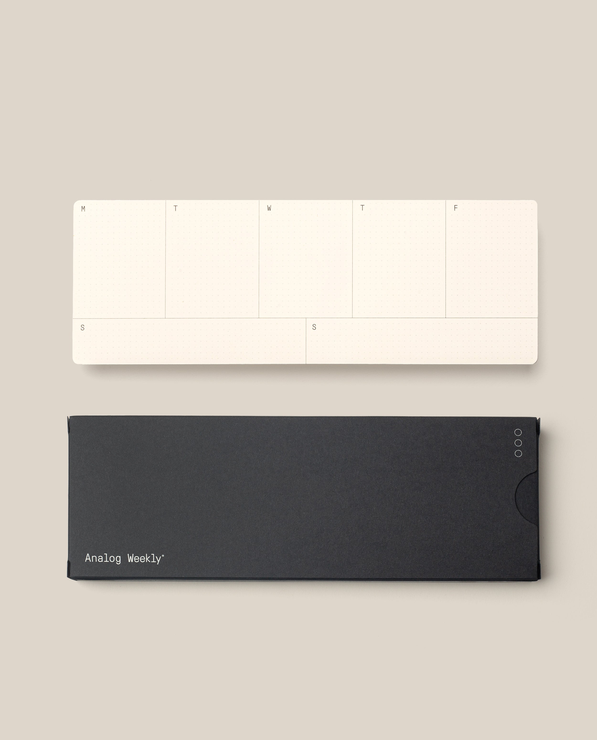 A minimalist, cream-colored Analog Weekly Cards pad with days labeled M to F and S on both ends sits above a closed black case on a beige background.