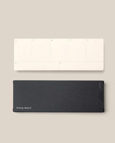 A minimalist, cream-colored Analog Weekly Cards pad with days labeled M to F and S on both ends sits above a closed black case on a beige background.
