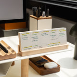 A modern desk setup features the Analog Weekly Planning Kit (Maple) displaying handwritten notes, with a tray for a phone and AirPods, and a pen holder. Sunlight streams in, creating a bright and organized workspace.
