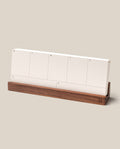 The Analog Weekly Planning Kit (Walnut) features a minimal desk weekly planner with blank white sections for each day, organized on stylish planner cards labeled with the days of the week by their initials. Set in a sleek walnut card holder and complemented by a light beige background, this kit brings both function and elegance to your workspace.