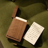 The Analog Bundle (Walnut)—a wooden kit with notecards, an open lid, and a refillable black and gold UGMONK pen—rests on a green cushion. A notecard lists tasks with "$27.25" at the top right corner.