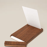 The Analog Bundle (Walnut) features a wooden kit with a sliding lid, shown partially open to display white index cards inside. A single card stands upright in the walnut holder against a plain light beige background.