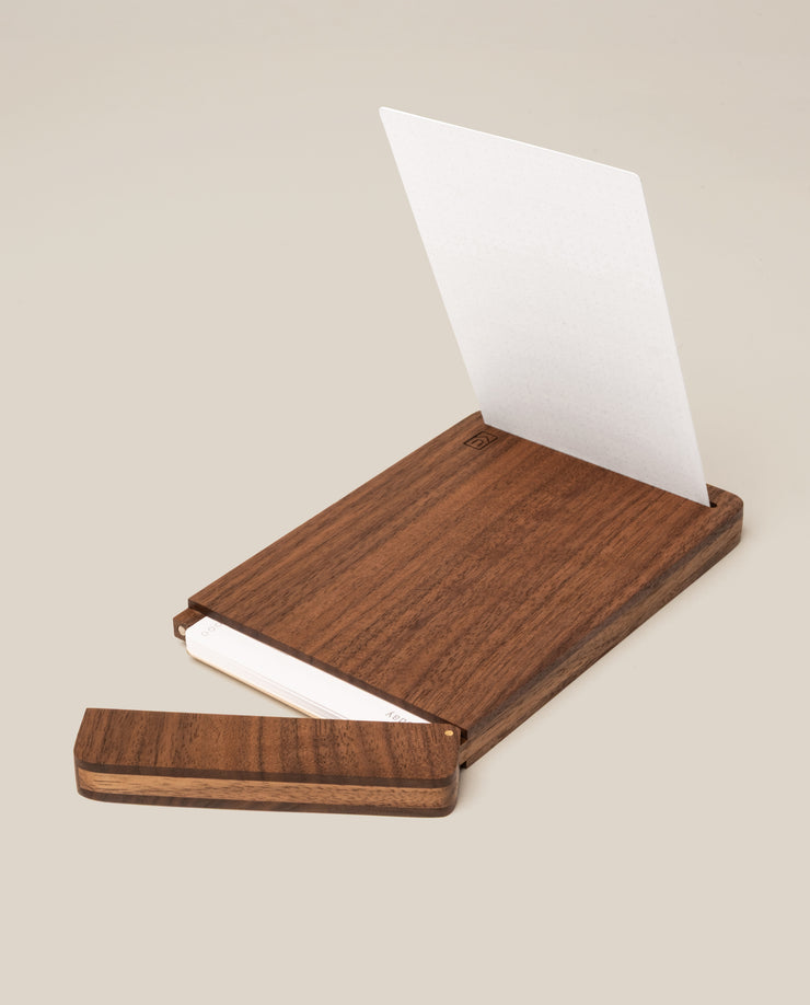 The Analog Bundle (Walnut) features a wooden kit with a sliding lid, shown partially open to display white index cards inside. A single card stands upright in the walnut holder against a plain light beige background.