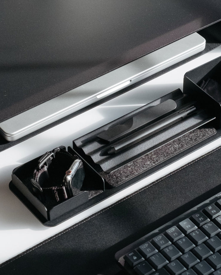 A close-up of a modern desk with a computer monitor, keyboard, and the Gather Zigzag Tray (2x1 - Black) holding two pens, plus another tray with a smartwatch—all neatly arranged on a black and white desk.