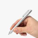 A hand holding the Craft Design Technology Multifunctional Pen, featuring a sleek silver design, against a plain white background.