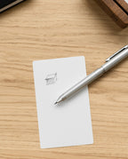 The Craft Design Technology Multifunctional Pen rests on a white notecard featuring a simple pencil sketch of a 3D box, all set atop a light wooden surface.