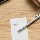 The Craft Design Technology Multifunctional Pen rests on a white notecard featuring a simple pencil sketch of a 3D box, all set atop a light wooden surface.