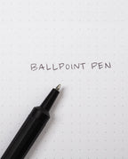 A sleek HMM Ballpoint Pen (Black) rests on dotted white paper with the words BALLPOINT PEN handwritten in black ink. This refillable pen combines elegant design with practicality, making it a standout aluminum ballpoint pen for everyday writing.