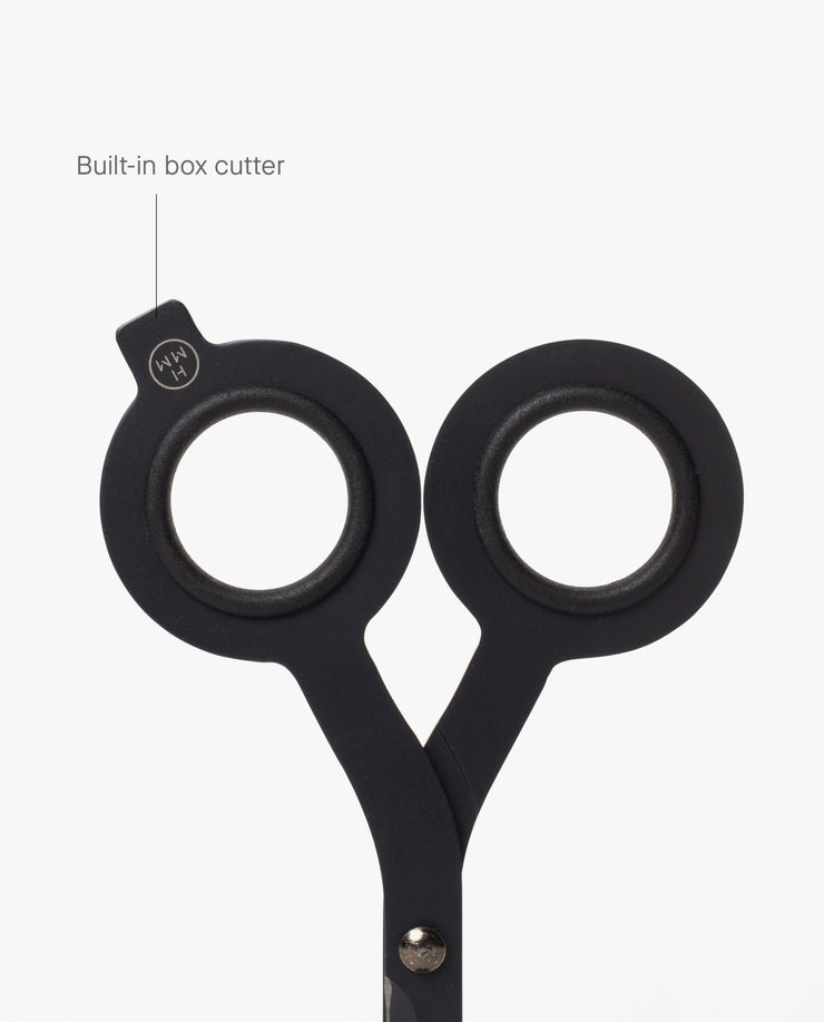 A close-up of HMM Scissors (Black) showcases their round handles, with one handle featuring a labeled built-in box cutter extending from the edge, all set against a white background.