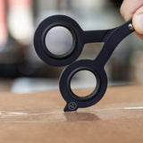 The HMM Scissors (Black), featuring a built-in box cutter, cut a piece of paper.