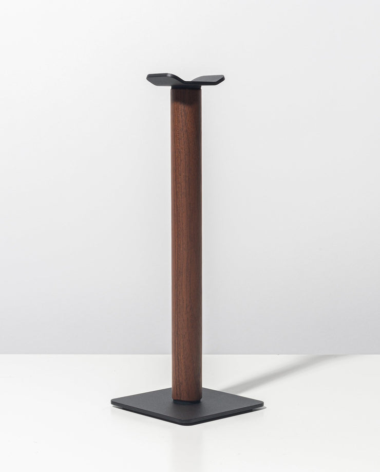The Gather Headphone Stand (1x1 - Black/Walnut) features a vertical walnut wood column, a square black powder-coated steel base, and a black metal platform, shown against a plain white background.