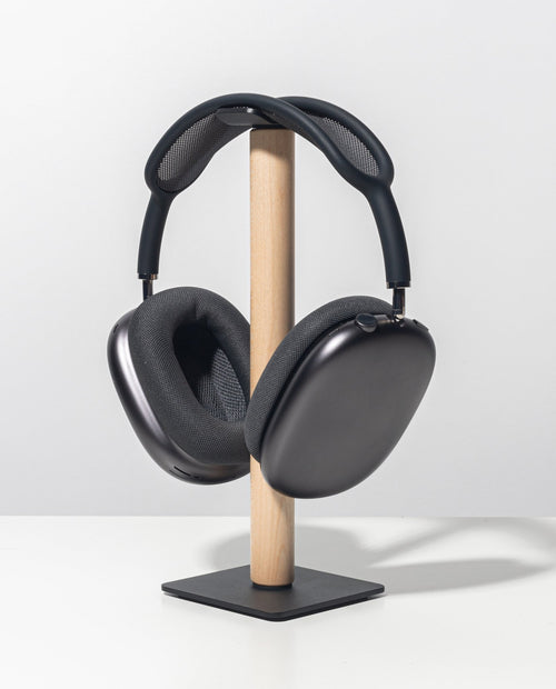 The Gather Headphone Stand (1x1 - Black/Maple), featuring a solid maple support and a powder coated steel square base, displays a pair of black over-ear headphones on a white surface against a plain light gray background.