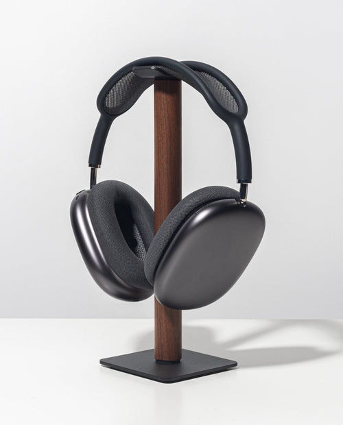 Sleek, over-ear black headphones with a mesh headband rest on the Gather Headphone Stand (1x1 - Black/Walnut), crafted from solid wood and powder-coated steel, displayed against a plain white background.