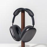 Sleek, over-ear black headphones with a mesh headband rest on the Gather Headphone Stand (1x1 - Black/Walnut), crafted from solid wood and powder-coated steel, displayed against a plain white background.
