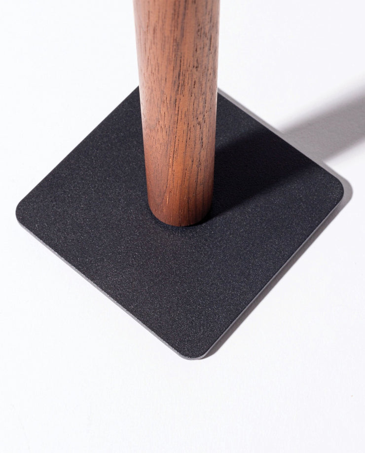 The Gather Headphone Stand (1x1 - Black/Walnut) features a solid walnut cylindrical pole set into a flat, black powder-coated steel square base, creating a minimalist look against a bright white background.