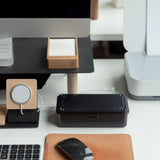 A neatly organized desk with a wireless mouse on a leather mouse pad, keyboard, monitor, note cards in a wooden holder, wireless charging pad, and the sleek Toyo Steel Stackable Storage Box T-190 (Black)—Made in Japan—beside a black box and part of a printer.