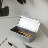 A Toyo Steel Stackable Storage Box T-190 (Silver) with its lid open sits on a white desk, holding a pencil and pen. In front are an open sketchbook, black marker, and scissors. A plant is in the background. Made in Japan.