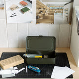 A Toyo Steel Stackable Storage Box T-190 (Military Green), made in Japan, sits open on a desk with a utility knife, Swiss army knife, cardboard box, and notecards. Above the workspace, mood board photos and materials are pinned to the wall.