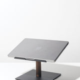 A closed silver Apple laptop sits on the Gather Laptop Stand (Black/Walnut), which has a black base and walnut support, placed on a white surface against a plain white background.